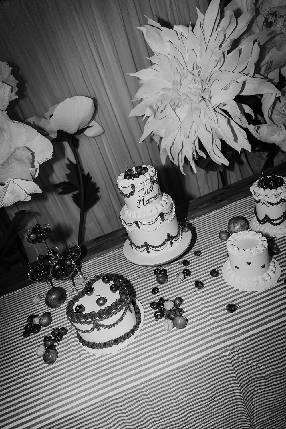 Vintage black and white photograph of elegant wedding cakes and floral decorations on a striped tablecloth.