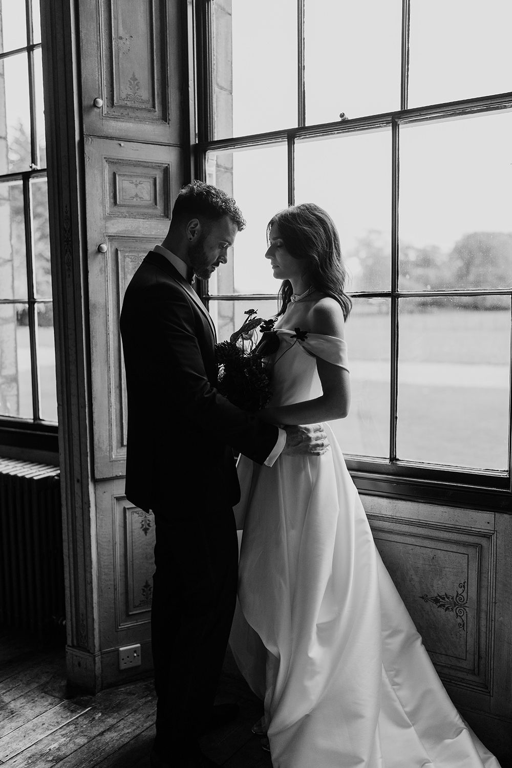 Bride and groom face towards each other while being lit by a grand window at Rise Hall.