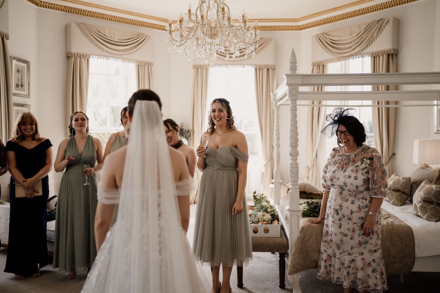 Bridesmaids stood facing the bride as they see her in her wedding dress for the first time, looking emotional.