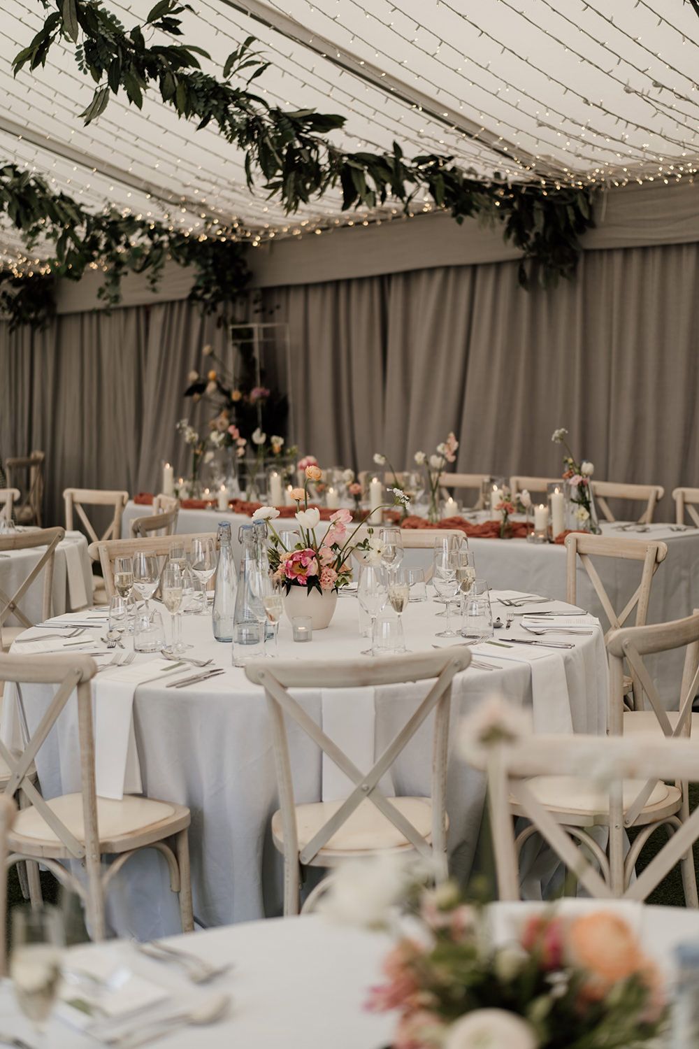 The wedding reception room at The Holford Estate ready for speeches, tables have white cloths with minimal flowers.