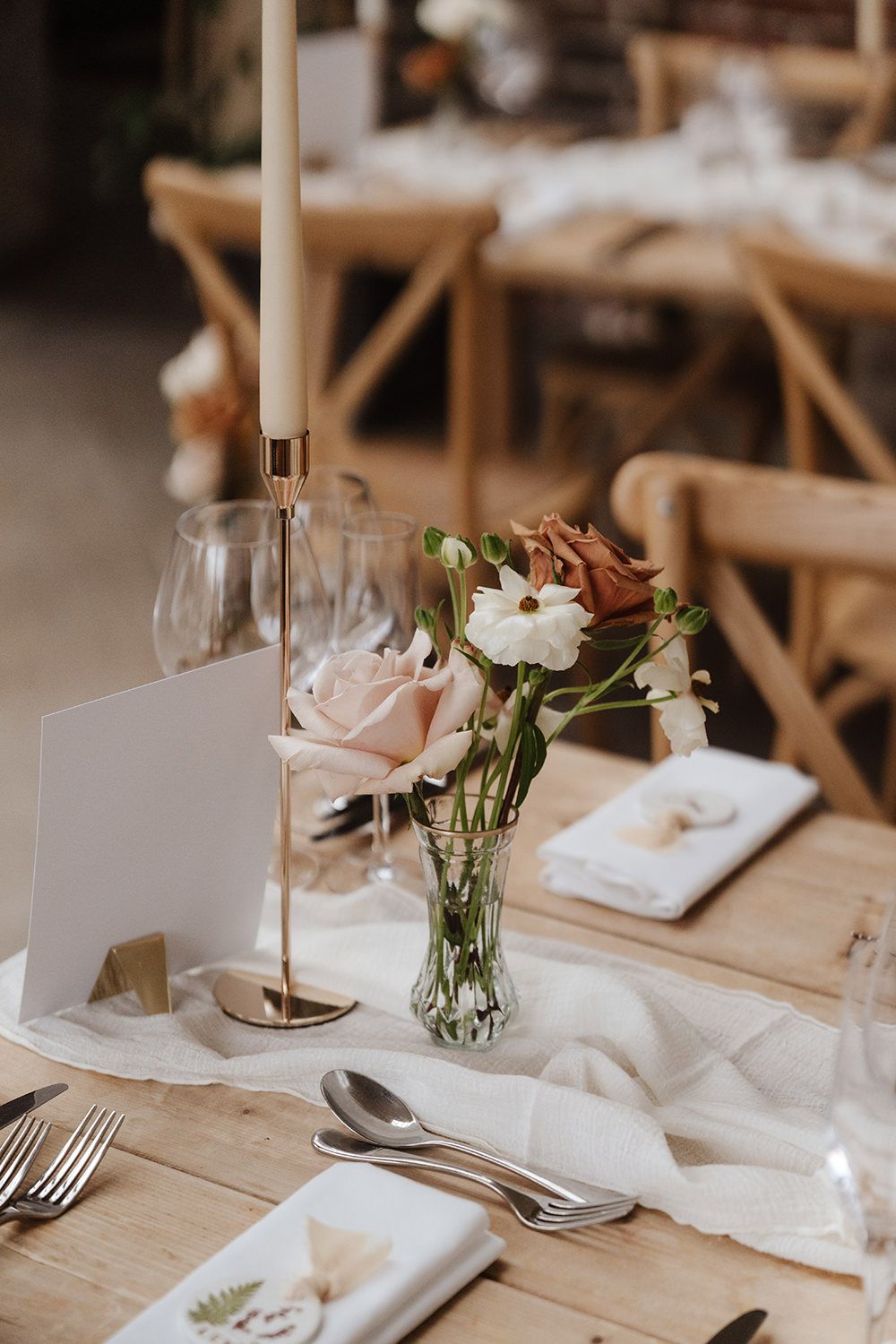 Elegant wedding table setting with rustic wooden chairs, delicate floral centerpiece, candles and wine glasses at a reception.