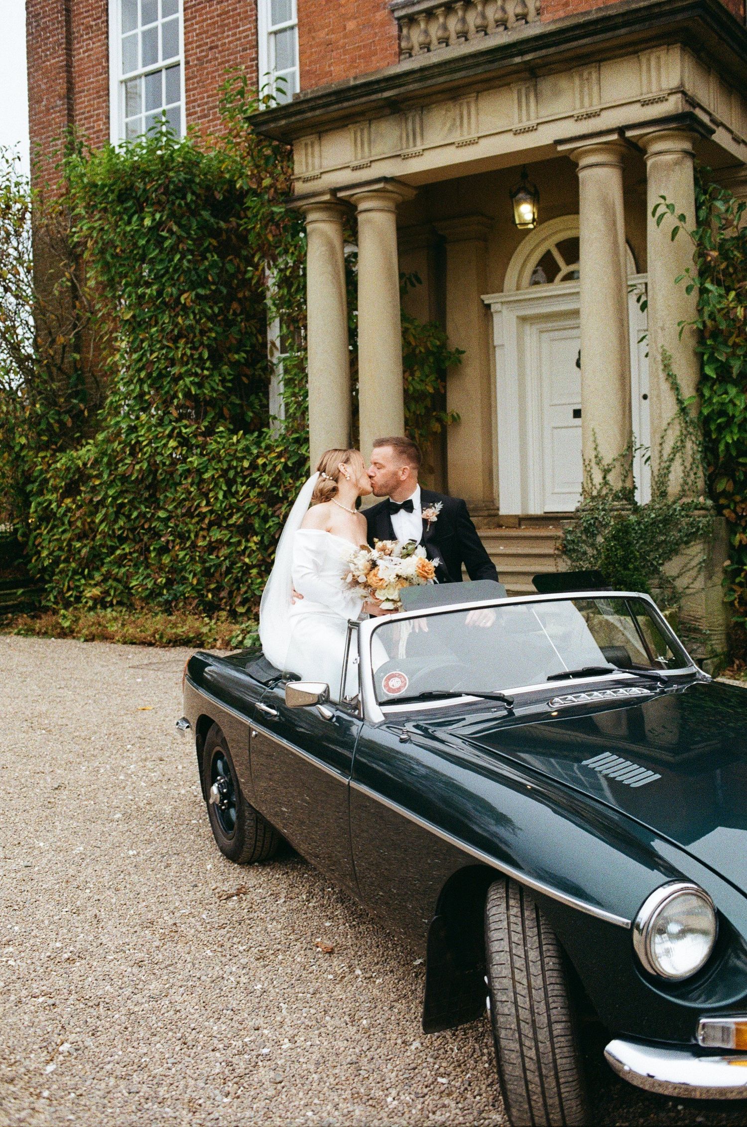 Classic black convertible car parked in front of a historic brick mansion with white columns.