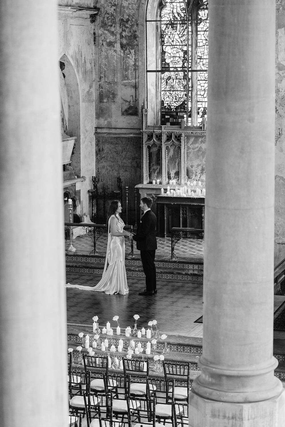 A black and white photograph shows a wedding ceremony inside a grand church with tall columns and rows of chairs.