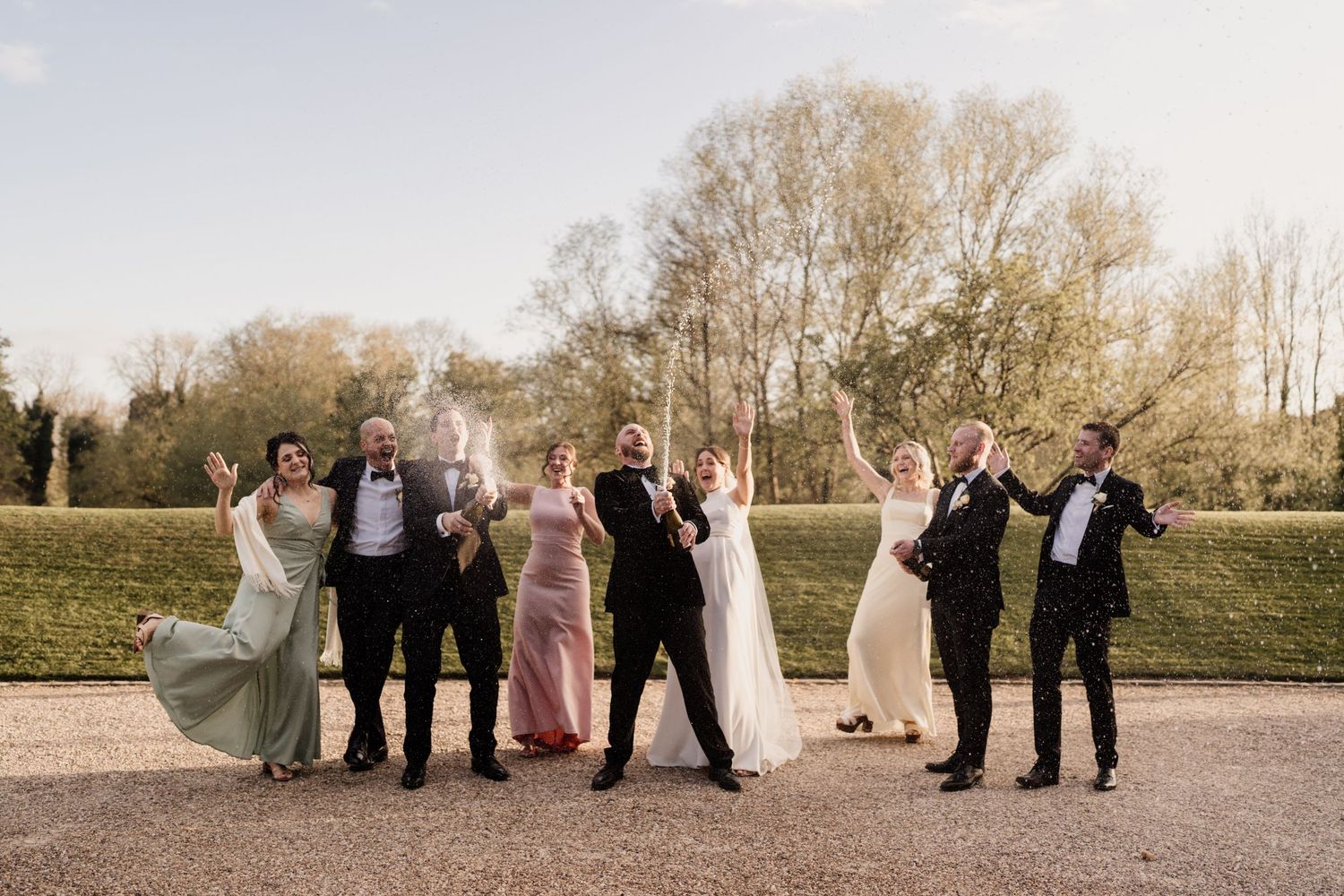 Celebratory group photo of wedding party jumping and posing against natural backdrop.