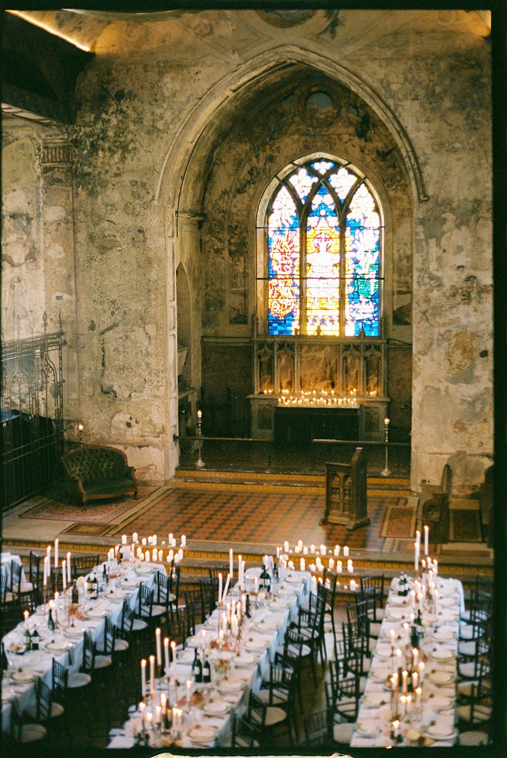 A gothic stone church interior set for a wedding reception with stained glass windows and candlelit tables.