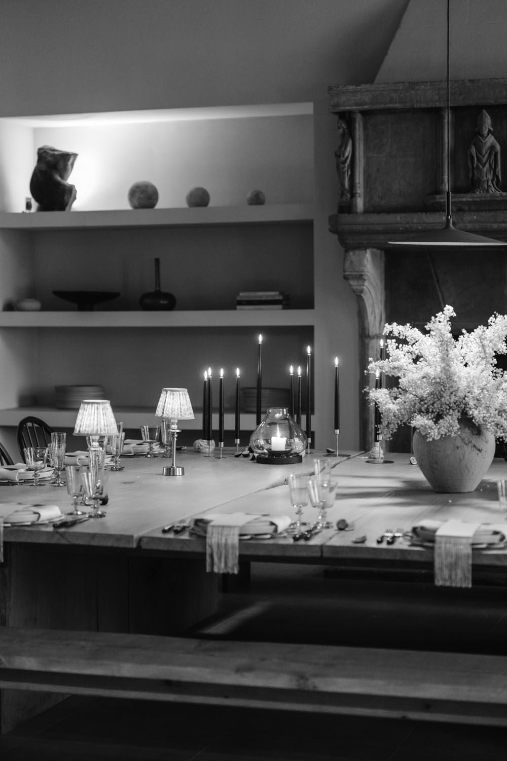 Elegant black and white dining table set with candles, glassware, and floral arrangement beside a rustic fireplace.