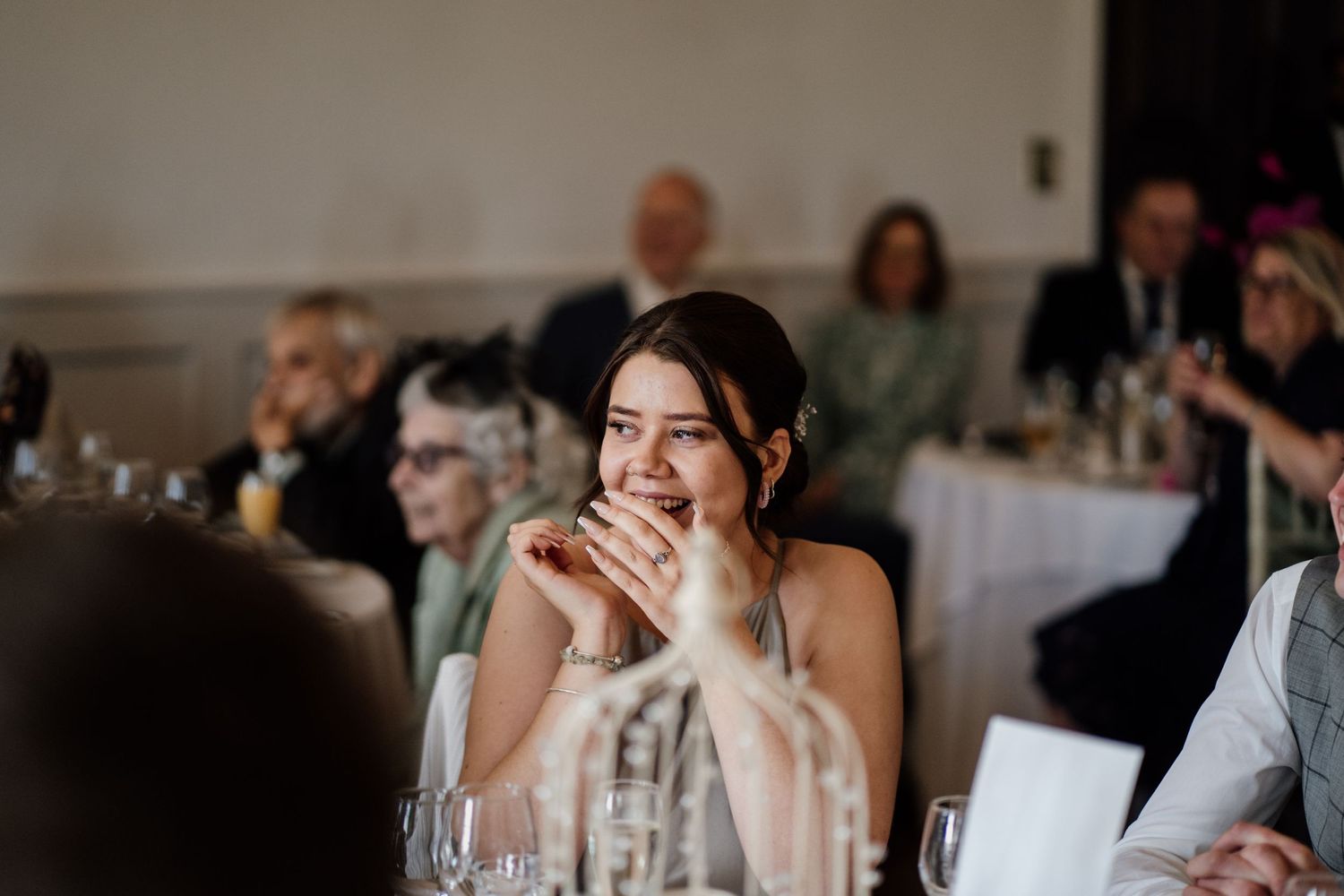 Emotional bridesmaid during wedding speeches with guests in the background.