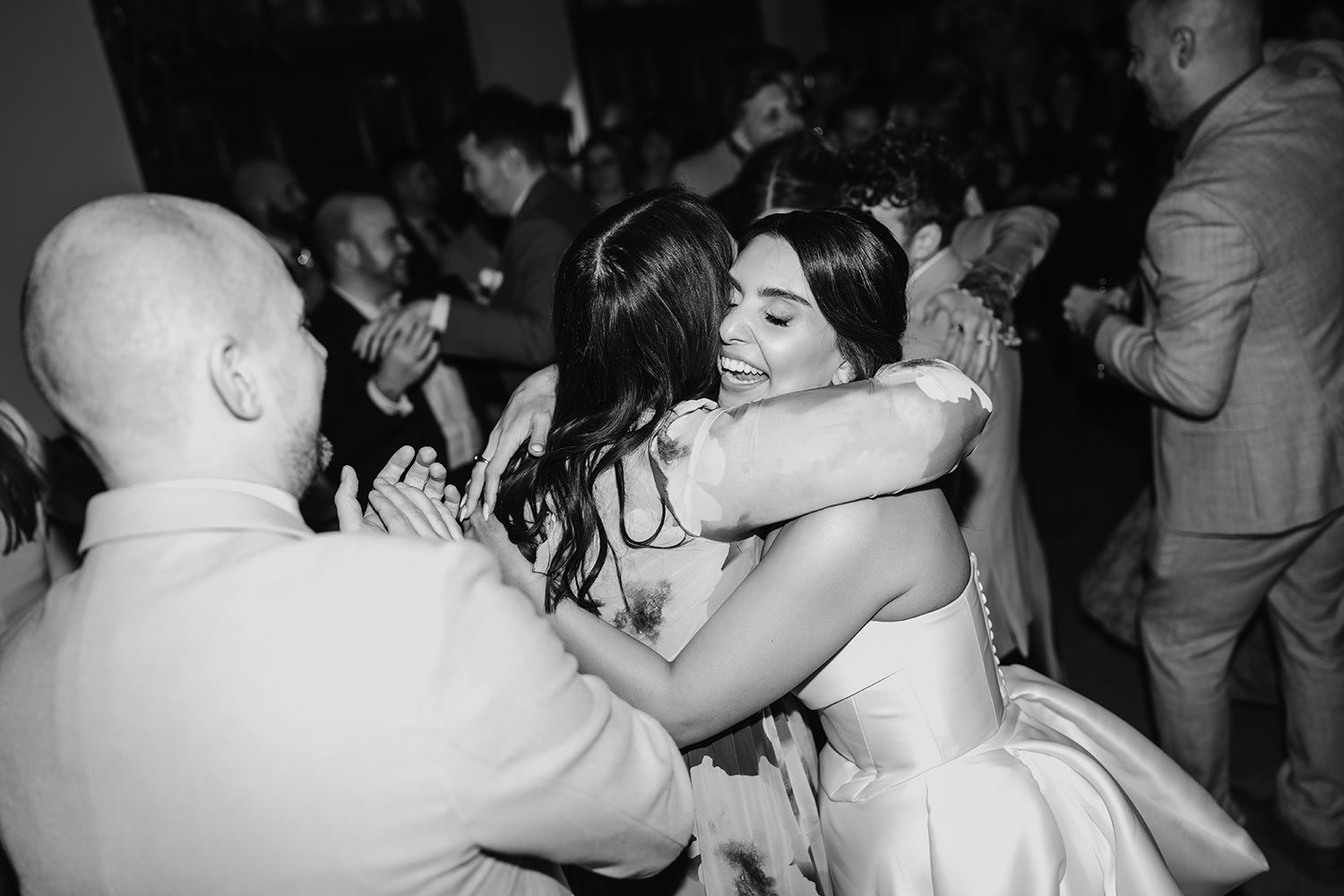 Black and white photo of people dancing and embracing at what appears to be a wedding reception or celebration.