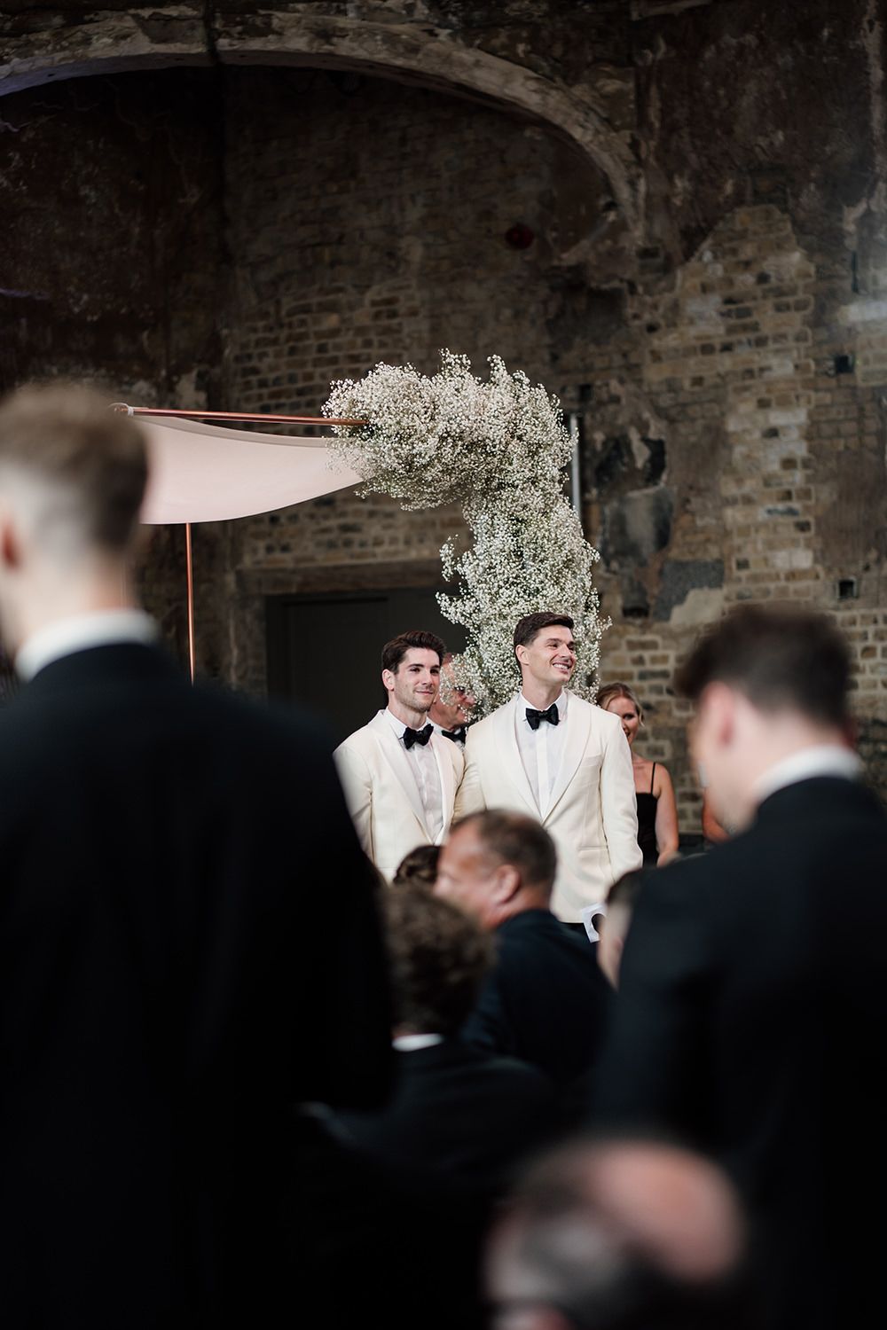 Grooms standing looking at their wedding guests.