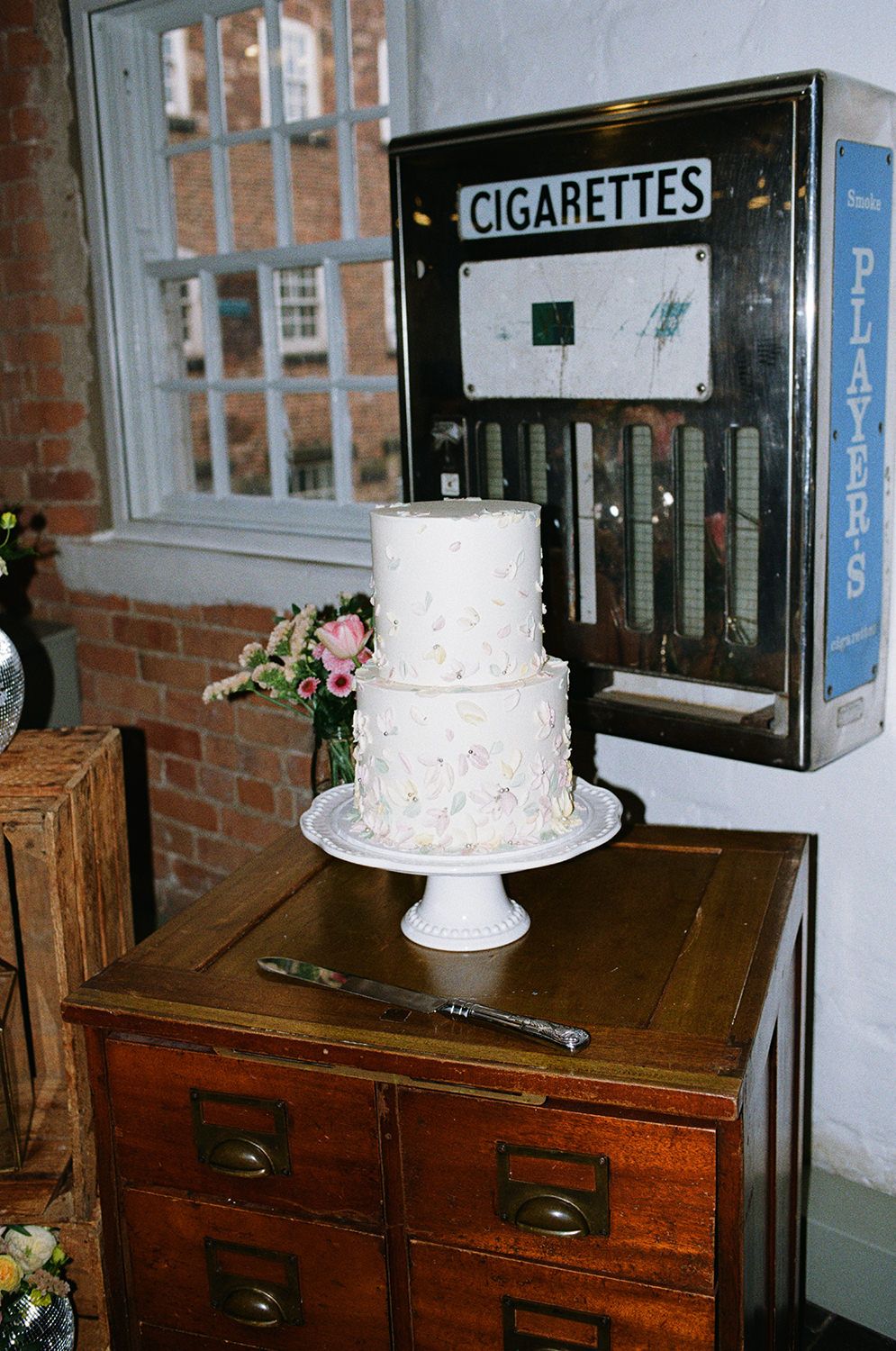 Wedding cake with pastel colours taken using flash with a retro cigarette machine behind.