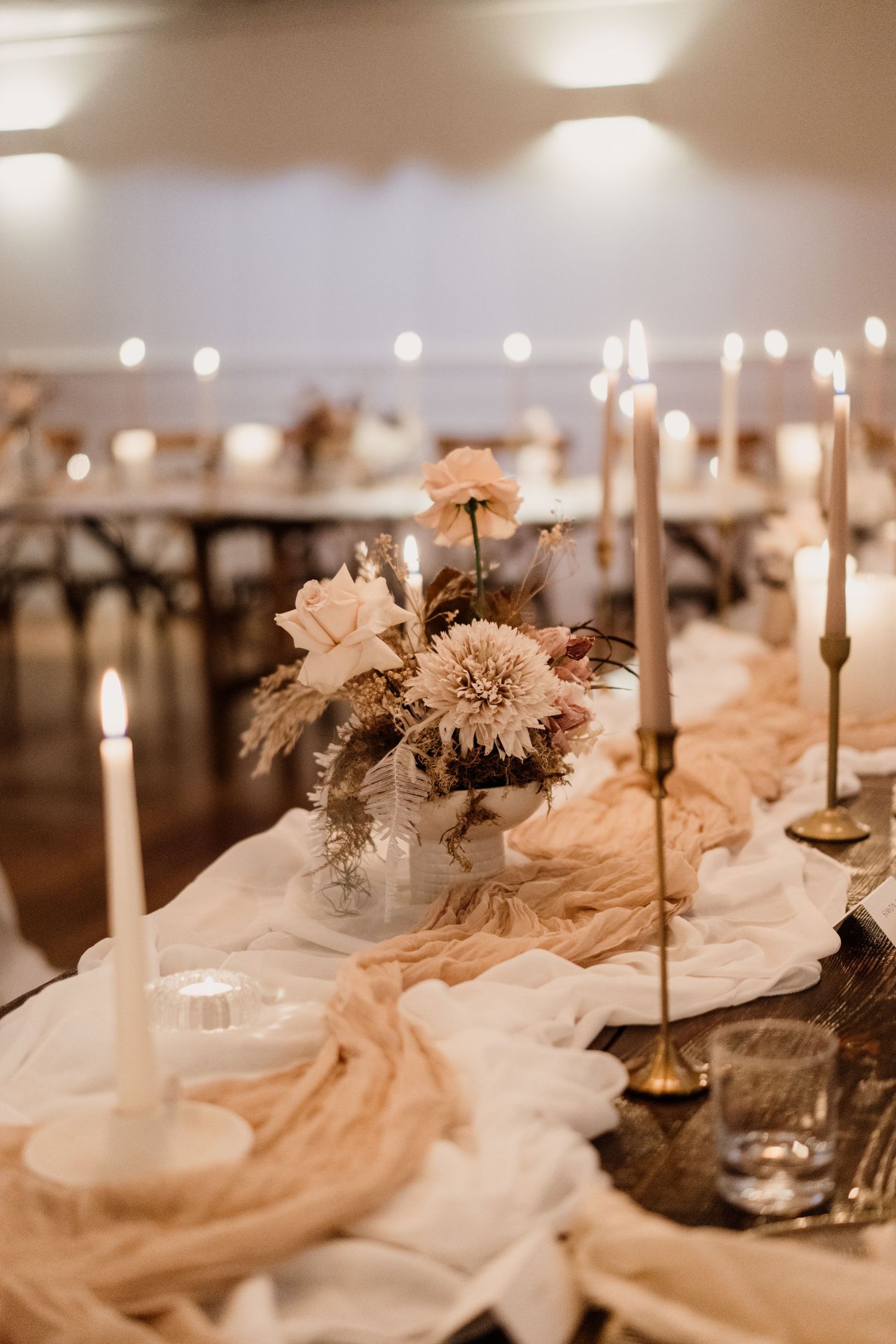 Romantic wedding table decor features blush flowers, flowing fabric, and glowing taper candles.