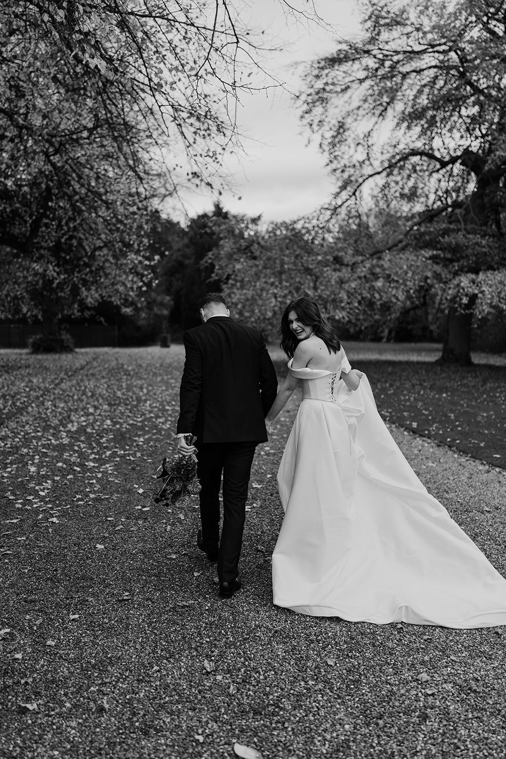 Bride and groom holding hands, smiling, laughing while working through the grounds of Rise Hall.