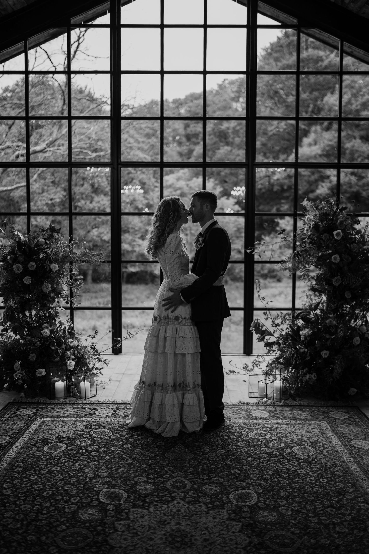 Couple kissing in front of barn windows with floral installations at either side on their wedding day.