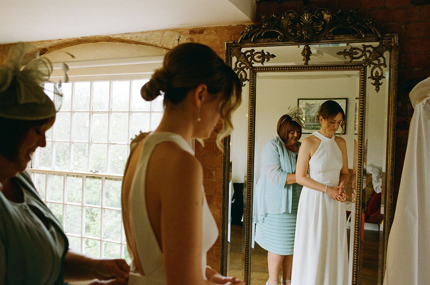 Brides mother fastening her white wedding dress in front of a mirror.
