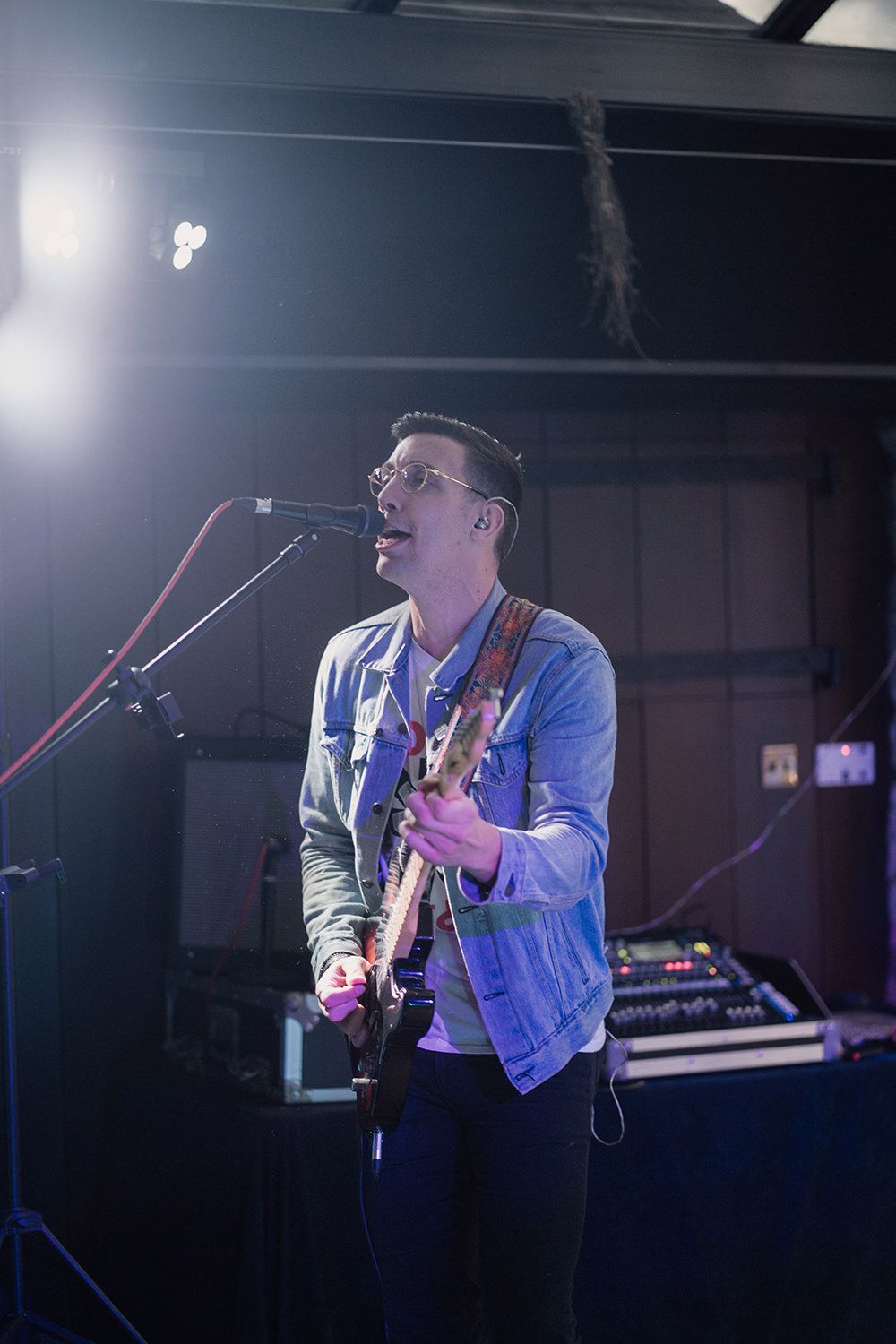Guitarist singing and playing his guitar, a microphone and a stage light are in-front of him.
