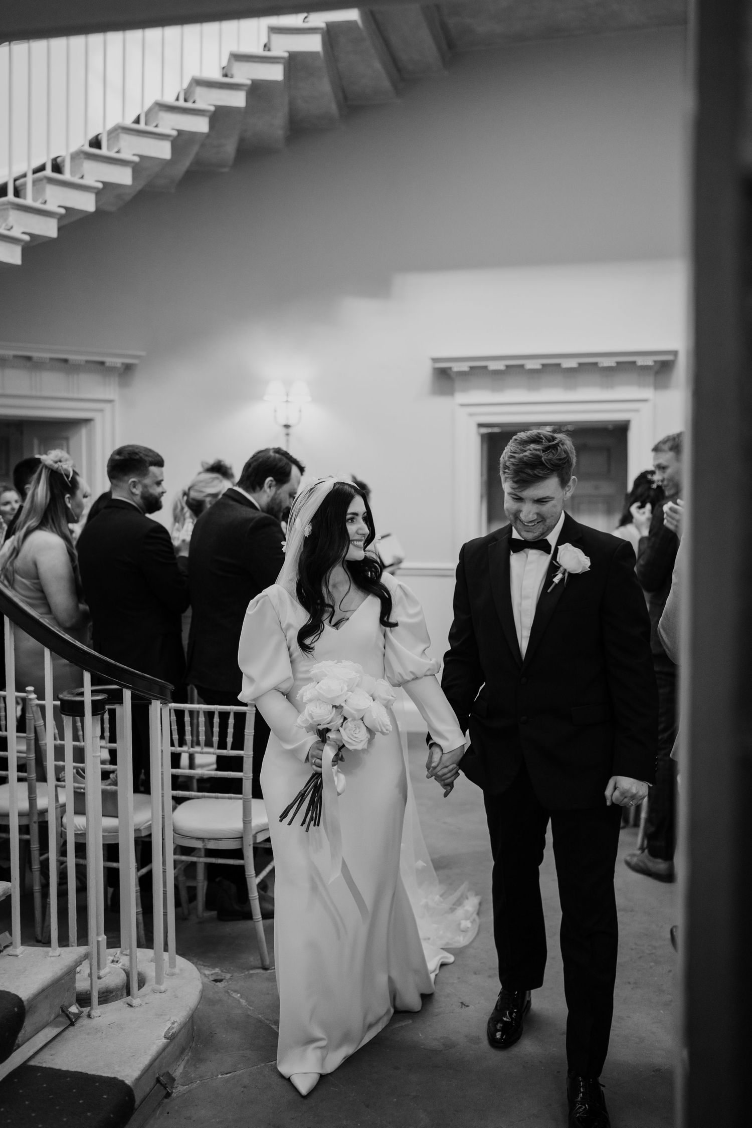 Bride and groom walking out of the ceremony room while holding hands and smiling towards eachother.