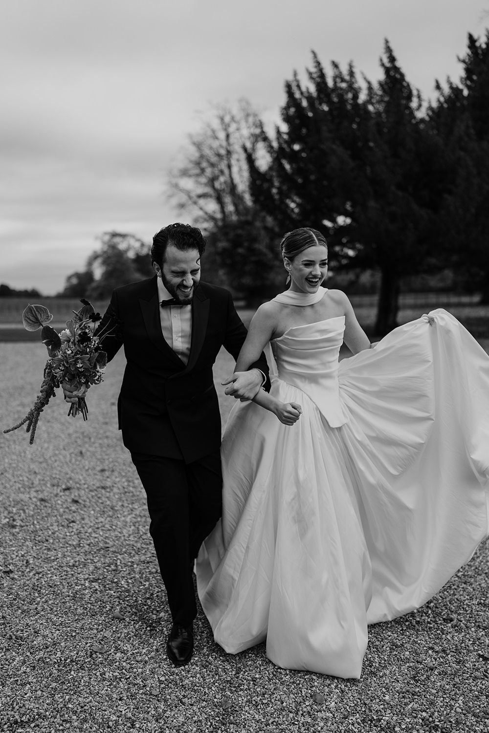 Bride and groom running in the grounds of Rise Hall, holding autumnal flowers while laughing and smiling.