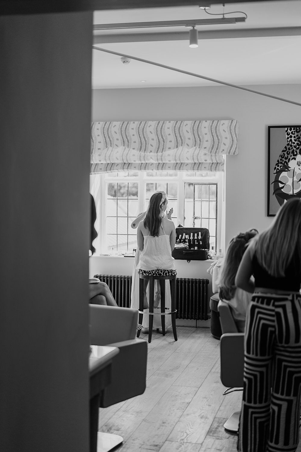 Bride in the getting ready room having her makeup done sat in front of a window.