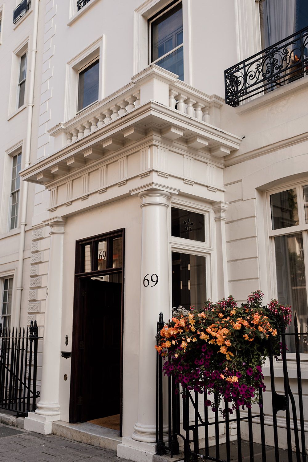 White townhouse entrance with black door number 69 and colorful flower boxes on ornate railings.