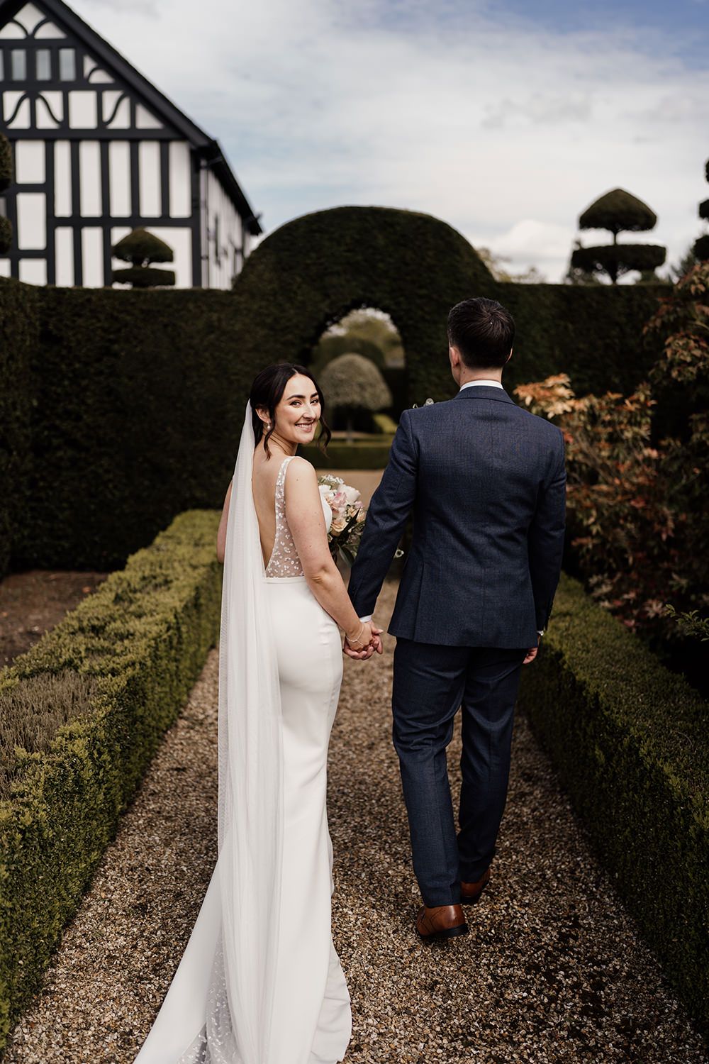 Bride and Groom walking and smiling through the gardens at The Holford Estate surrounding them.