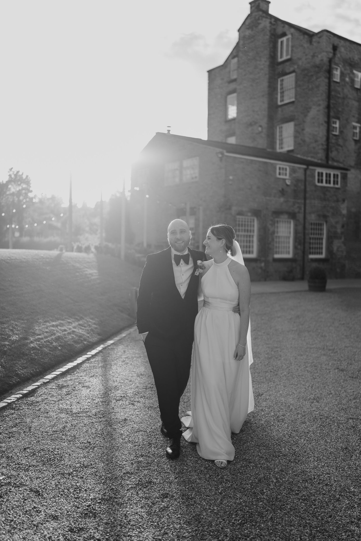 Romantic black and white portrait of couple outside historic brick building at sunset.