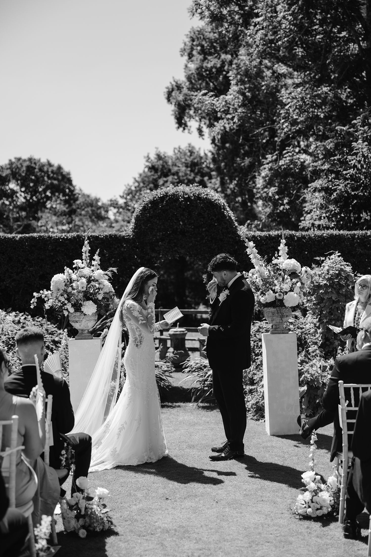 Black and white outdoor garden wedding ceremony with bride and groom exchanging vows beneath a floral arch.