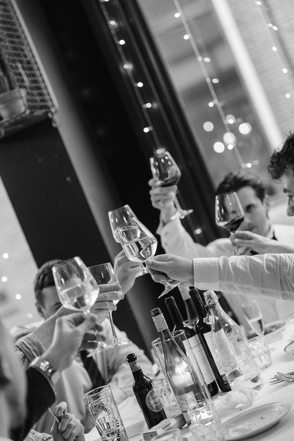 Black and white photo of wine glasses and bottles arranged on an elegant dining table with bokeh lights in background.