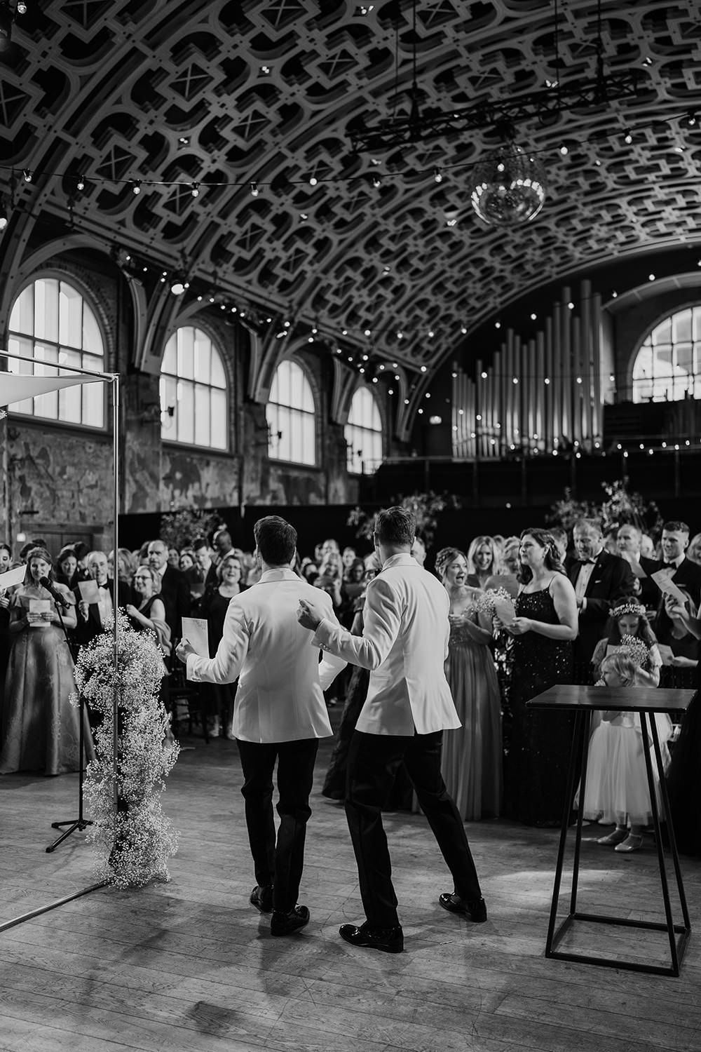 Grooms performing to their guests during the ceremony with the architecture of Battersea arts centre.