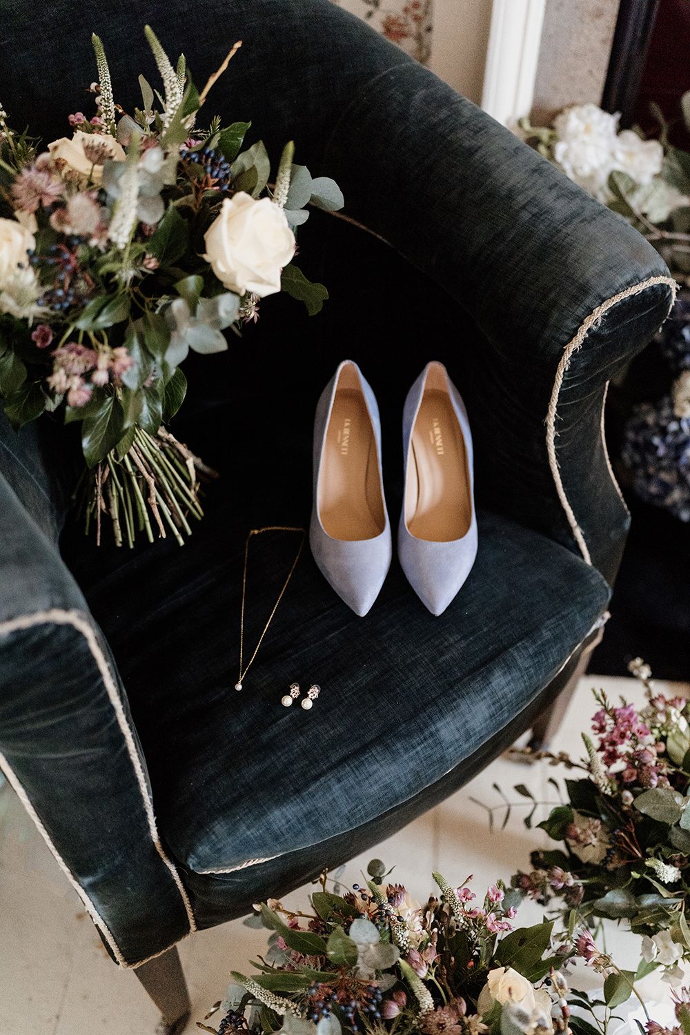 Blue wedding shoes on blue chair surrounded by wedding flowers.