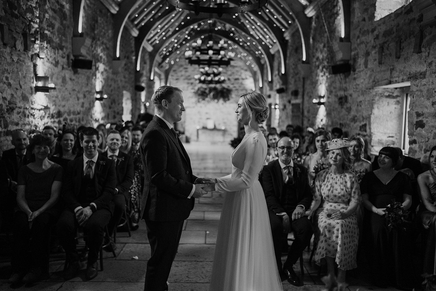 Bride and groom face towards each other at their wedding ceremony at Healey Barn with guests in the background.