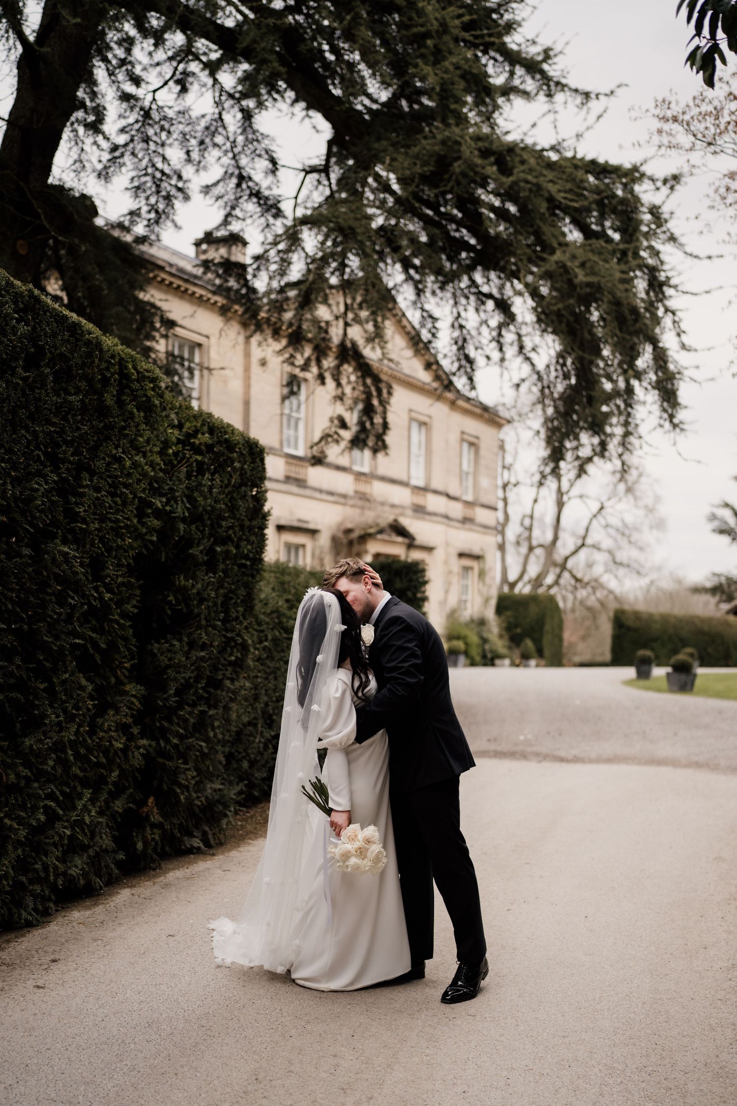 Bride and groom kissing at Middleton Lodge Estate with the main house and trees behind them.