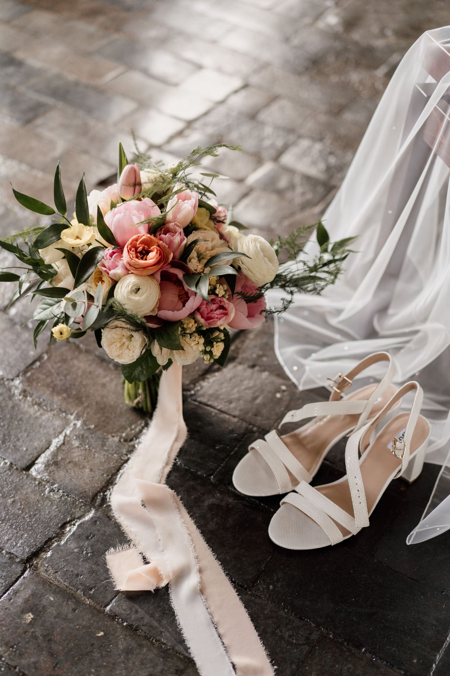 Wedding bouquet with pink roses and white shoes on stone floor.