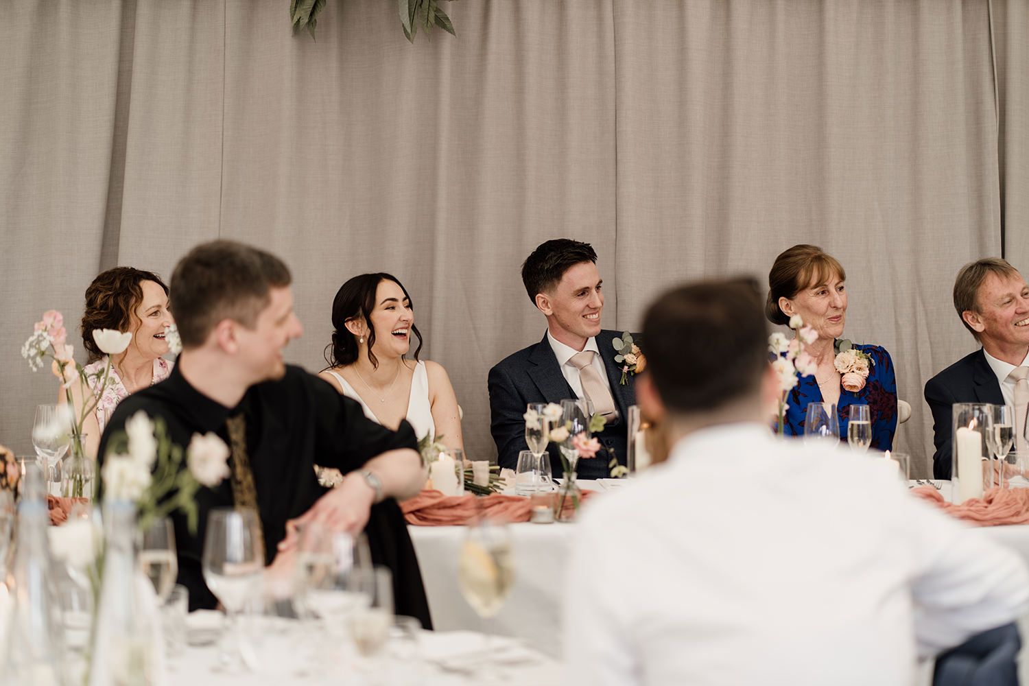 Bride and Groom laughing during wedding speeches with guests sat watching.