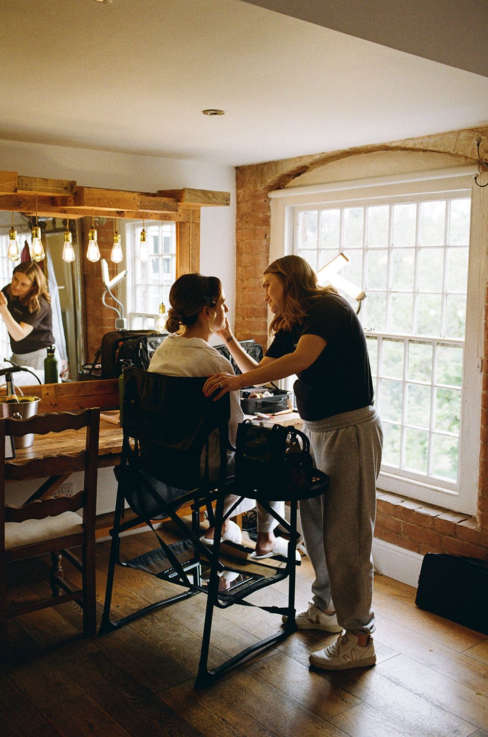 Bride sat in makeup chair in front of an old mill window.