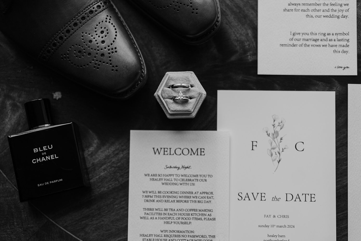 Black and white image of grooms shoes, wedding stationery and wedding rings.