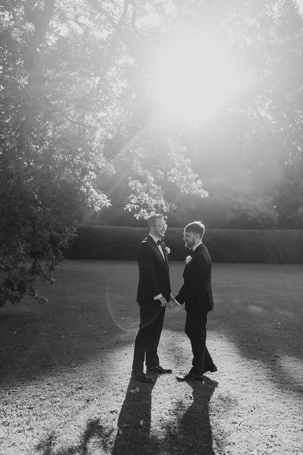The grooms stealing a quiet moment in the gardens, framed by the evening light.