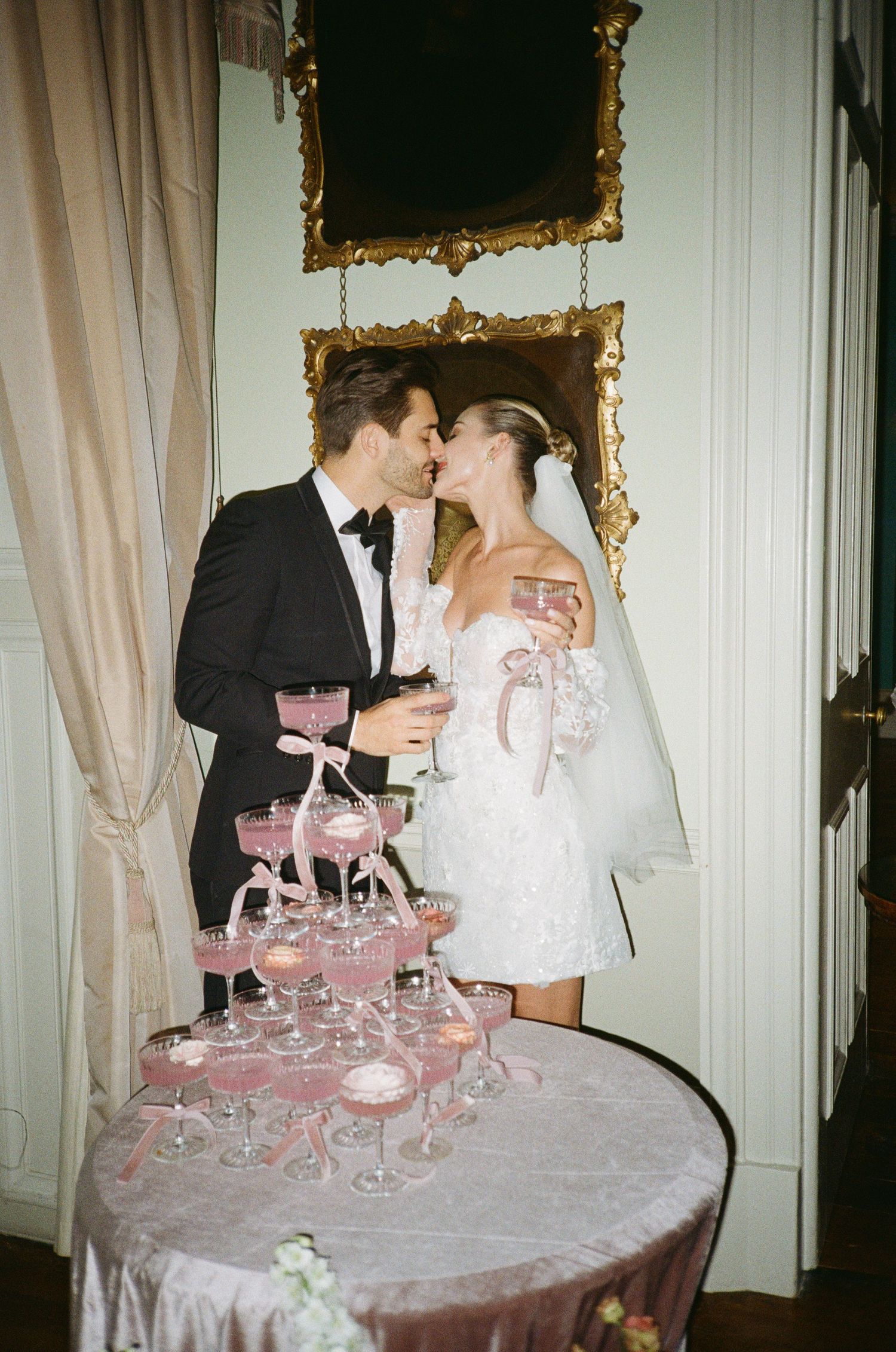 A couple shares a romantic moment by a champagne tower at their wedding reception in an elegant room with ornate mirrors.