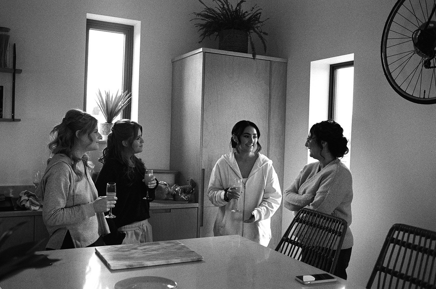 Black and white image of bride and bridesmaids stood talking on her wedding morning.