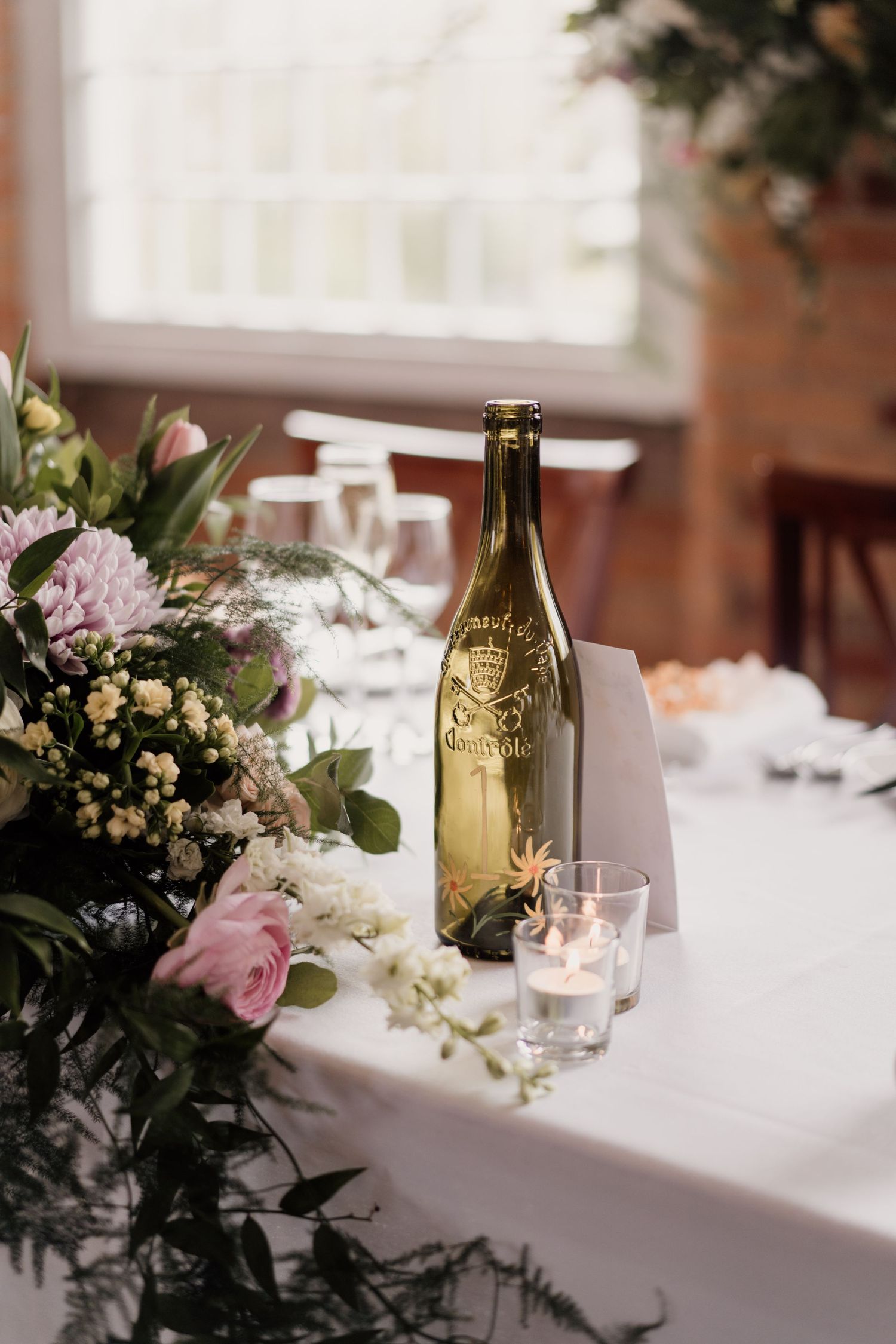 Elegant floral centerpiece with pink roses and decorative wine bottle on white tablecloth.