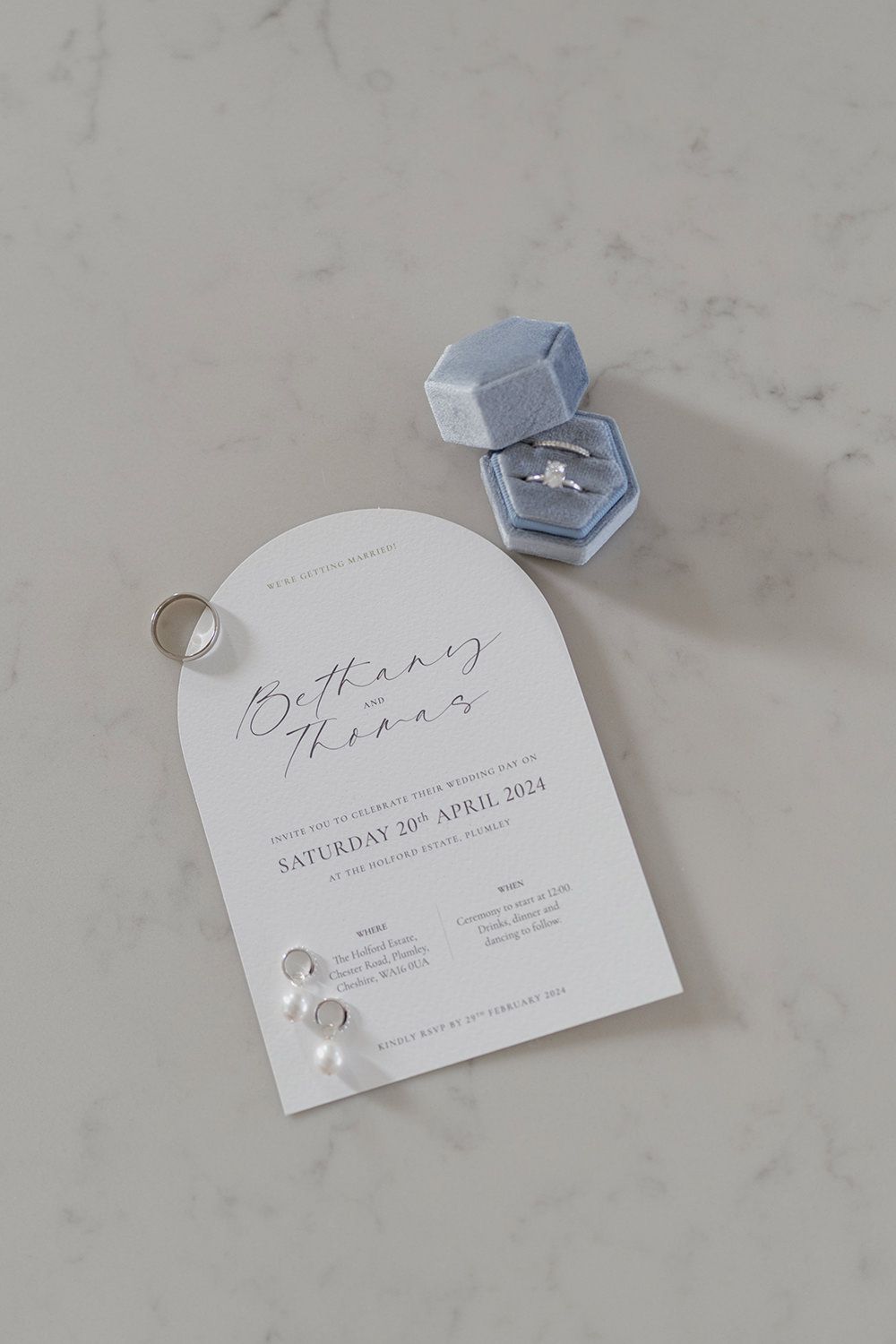 Wedding invite on marble background with weddings rings and jewellery.