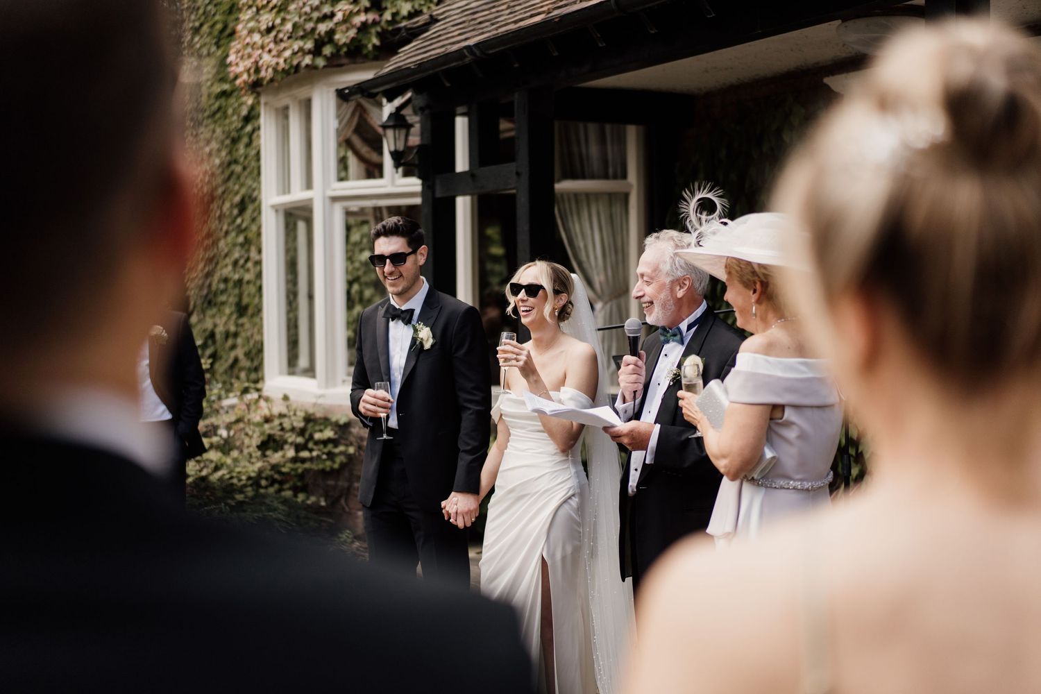 Bride and groom smiling with family outside an ivy-covered venue during their wedding drinks reception.