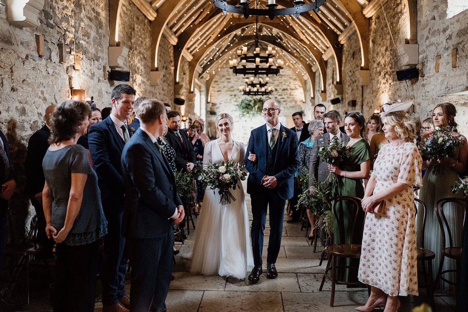 Bride walks down the aisle at her wedding while linking arms with her father.