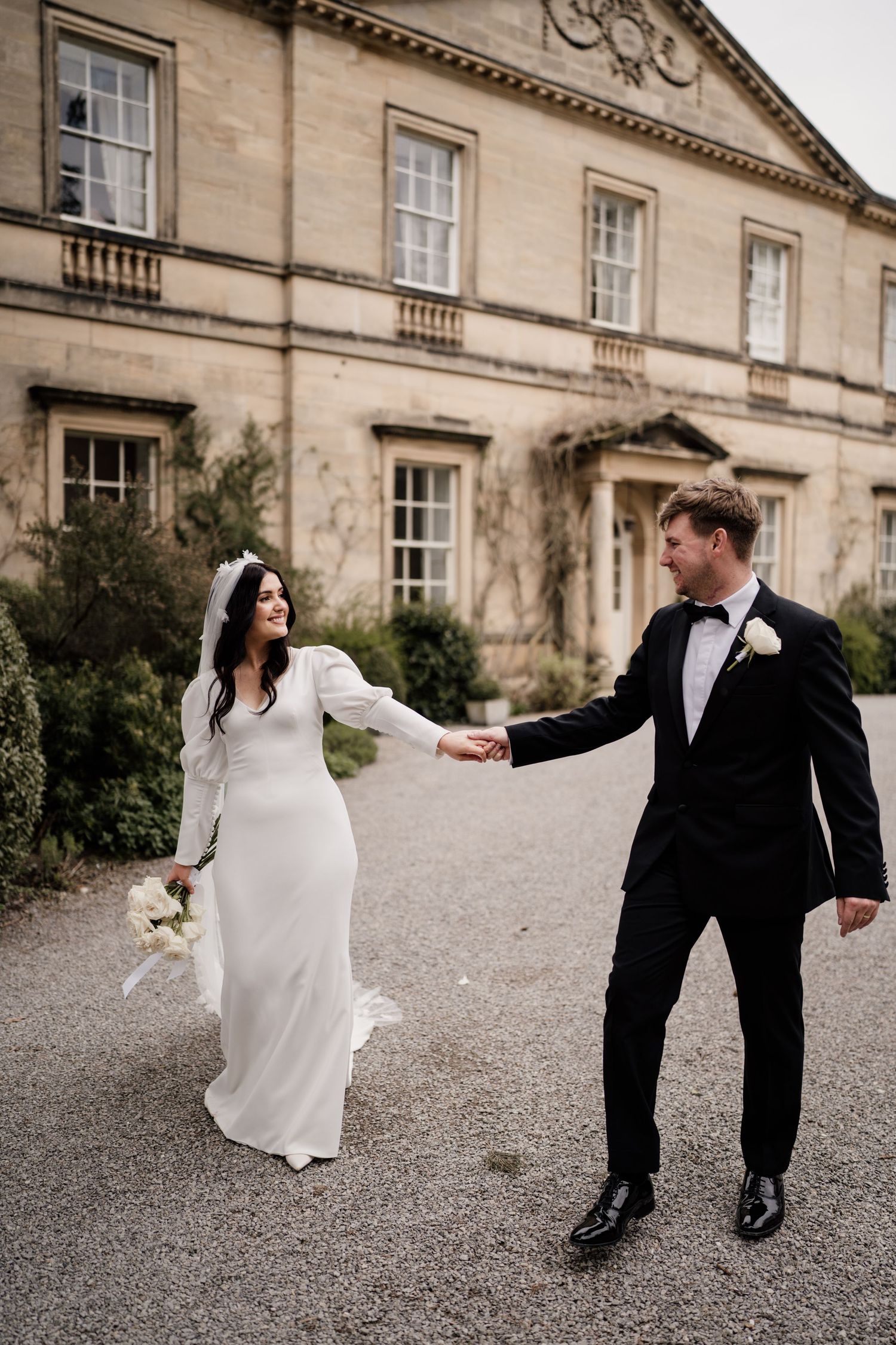 Bride and groom holding hands looking towards eachother at Middleton Lodge Estate with the main house behind.