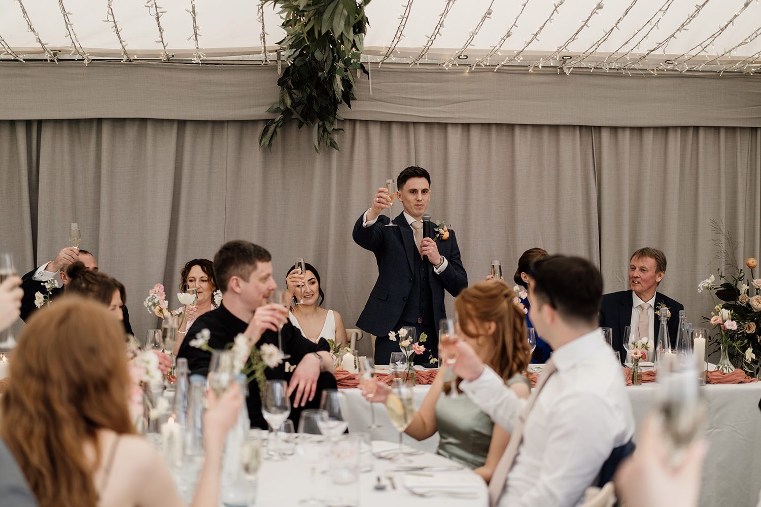 Groom making a toast during his speeches with guests sat at tables watching.