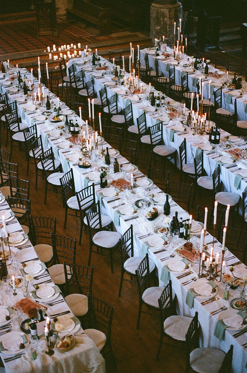 Elegant wedding reception tables with white linens, tall candelabras, and black chiavari chairs arranged in long rows.
