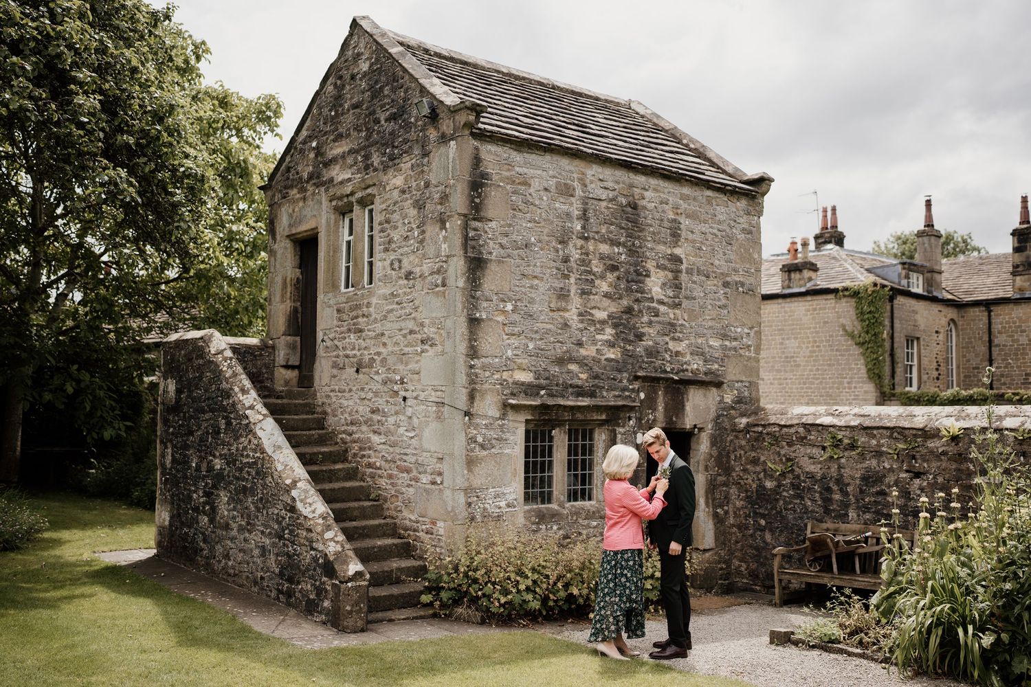 Couple shares romantic kiss beside charming stone building during outdoor wedding celebration.