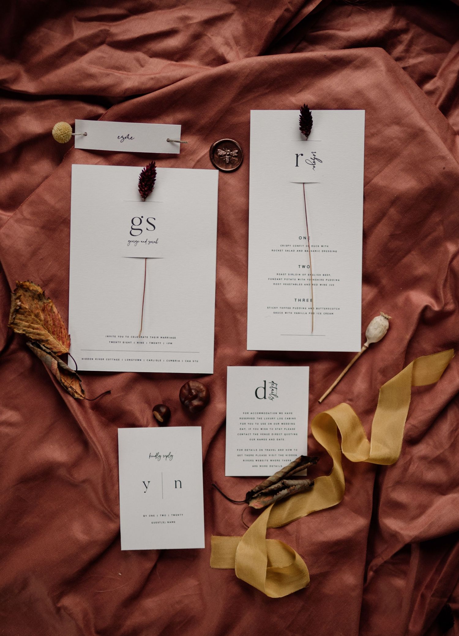 Editorial wedding stationery styled on a rust fabric with dried flowers.