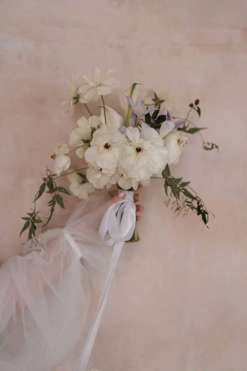 Bride holding flowers against limewash wall at Els Comellars.