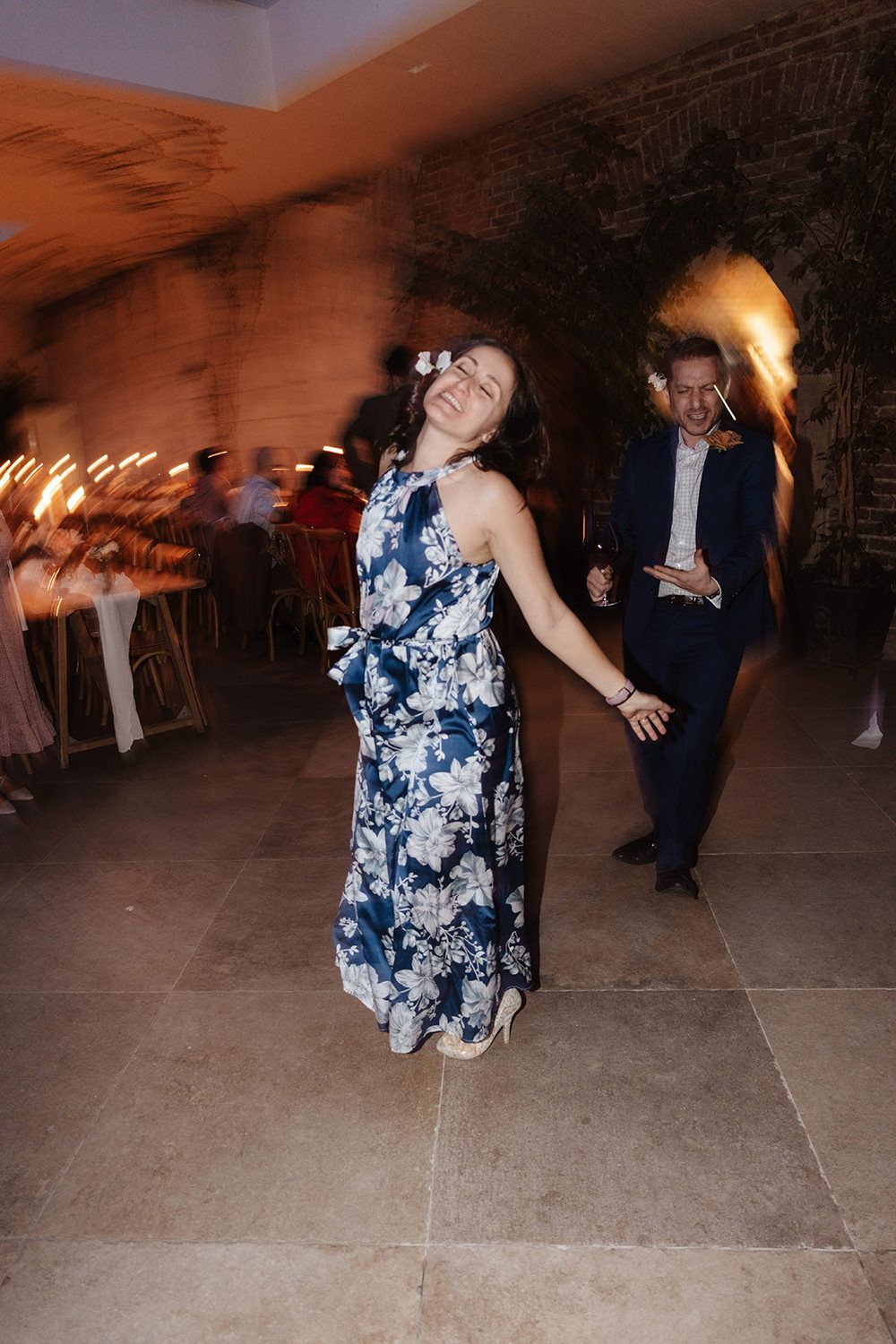 People dancing and having fun at a party, with someone wearing a blue floral dress moving energetically on the dance floor.