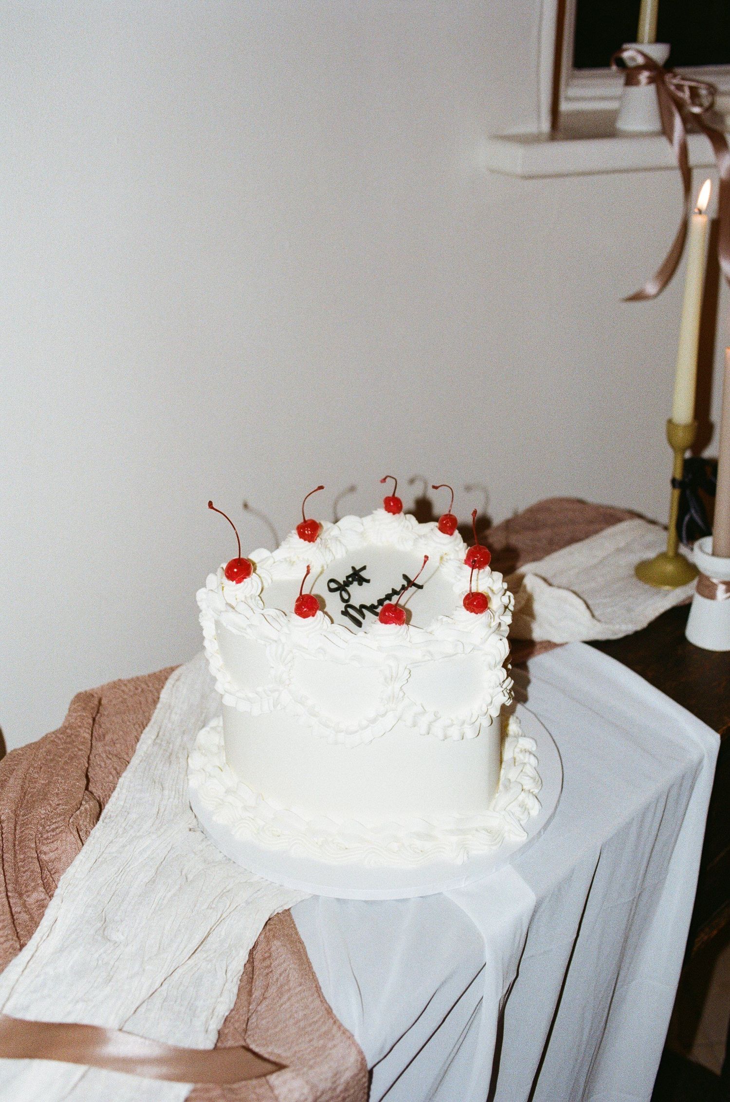 White wedding cake decorated with cherries and whipped frosting on a tablecloth.